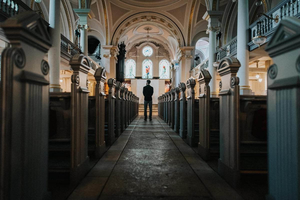 A man standing alone in the aisle of a large church